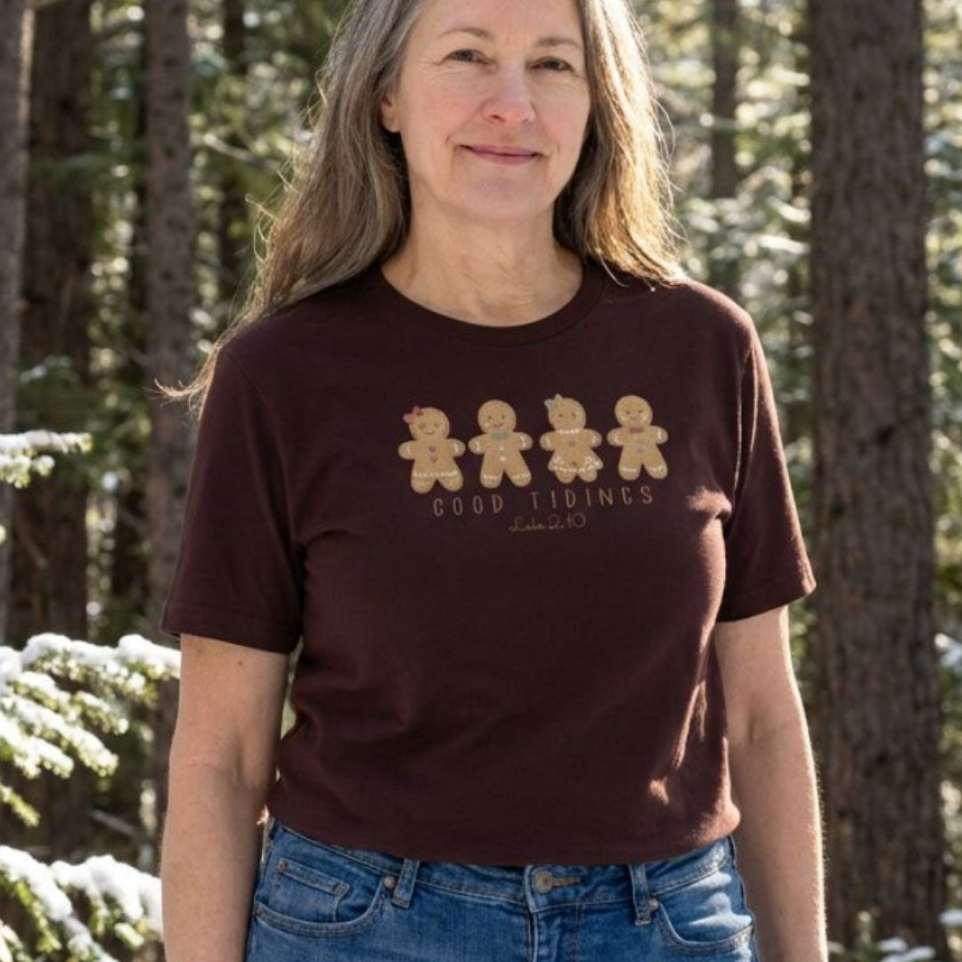 Christian Christmas tee with four gingerbread characters in a printed faux embroidery style, with Good Tidings and Luke 2:10 underneath.