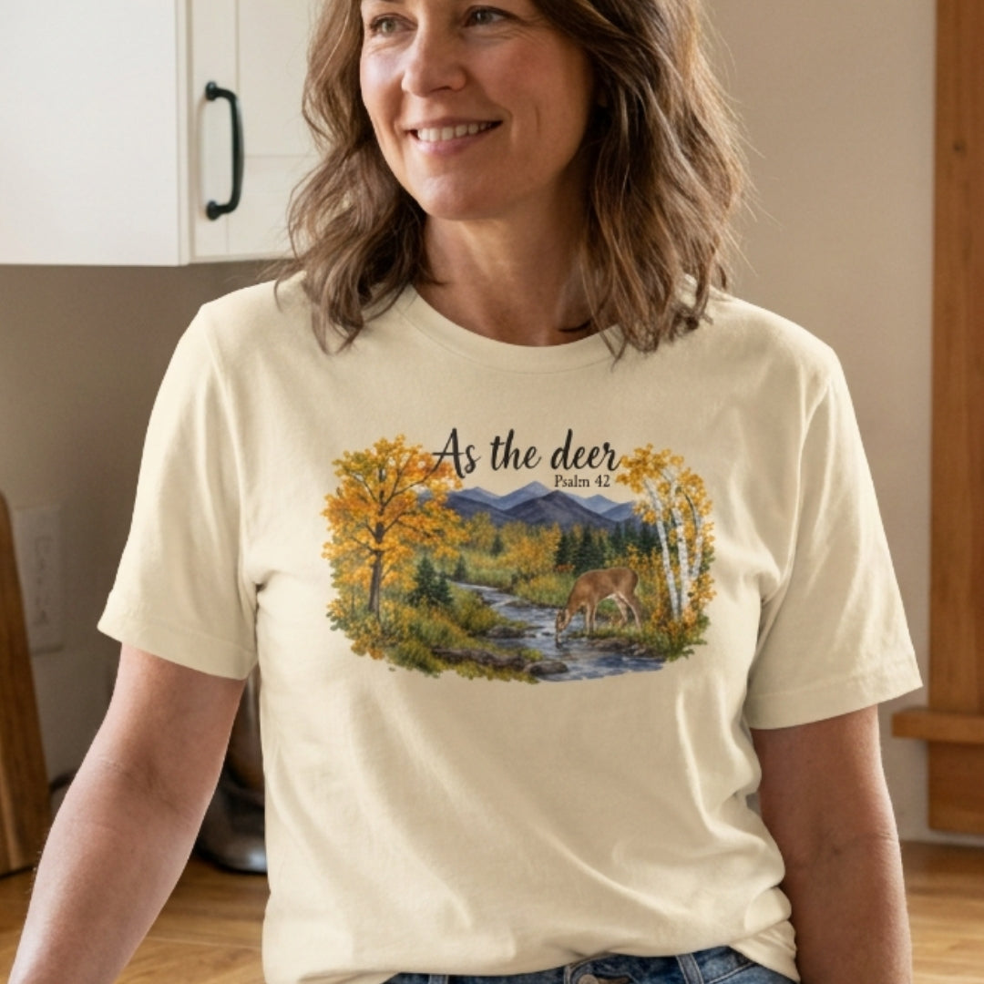 A woman wearing a cream-colored t-shirt with a graphic print of a deer in an autumn forest by a river, with the text 'As the deer Psalm 42'.
