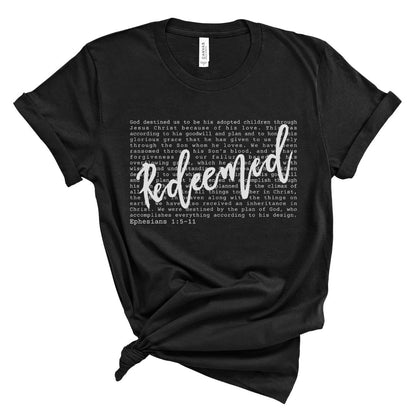 Black Christian women’s t-shirt with the word “Redeemed” in white script lettering layered over Ephesians 1:5–11 scripture text. Minimalist faith-based tee with a soft, relaxed fit.