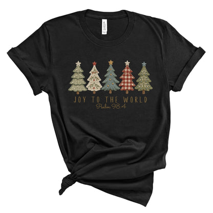 A black short-sleeve t-shirt with a graphic of five patterned Christmas trees and the text 'JOY TO THE WORLD Psalm 98:4' printed on the front, styled with a knot at the bottom hem on a white background.
