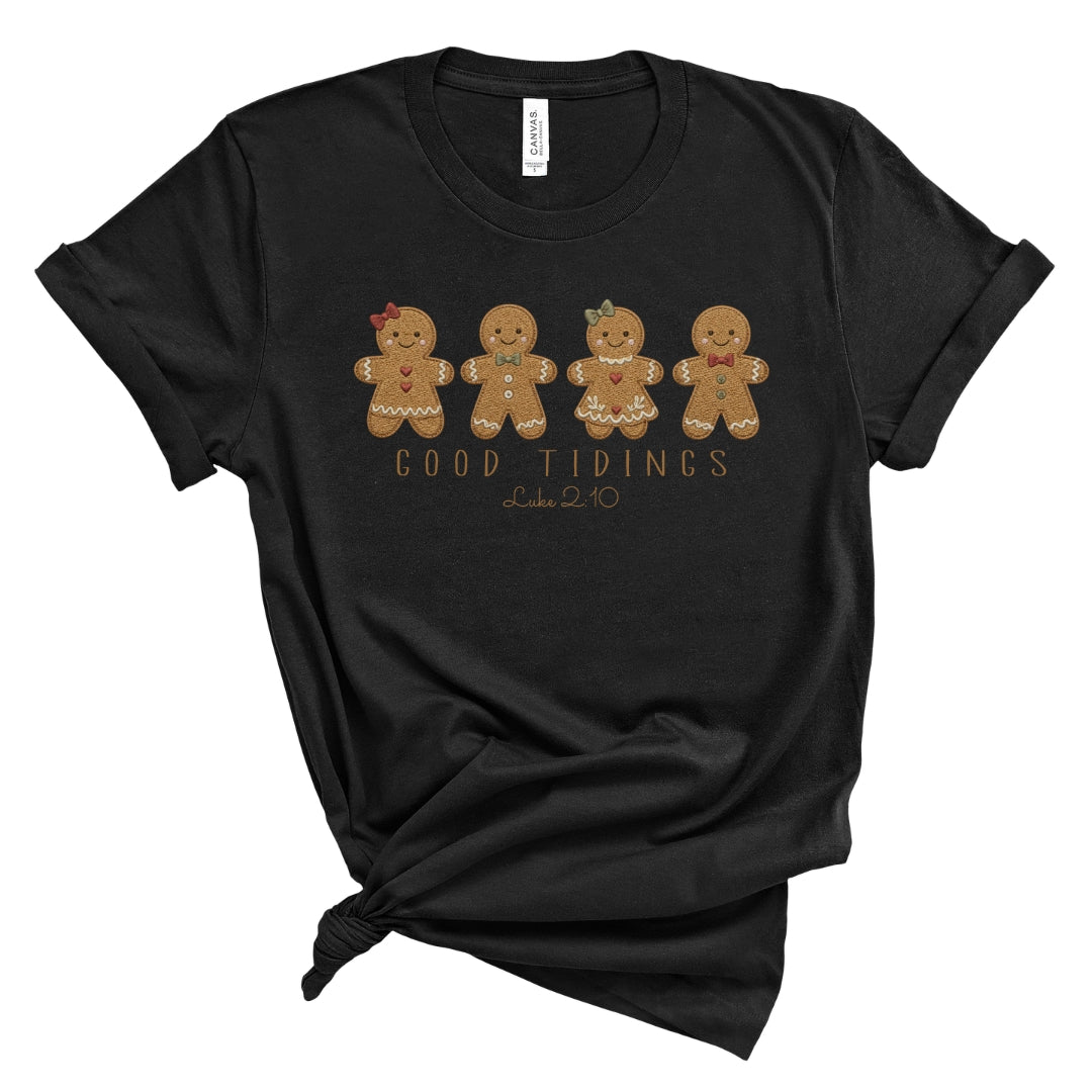 Christian Christmas tee with four gingerbread characters in a printed faux embroidery style, with Good Tidings and Luke 2:10 underneath.