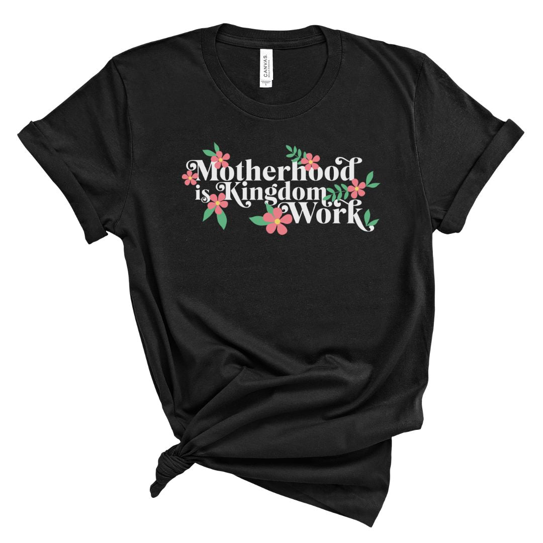 Black crew neck t-shirt with the text 'Motherhood is a Kingdom Work' surrounded by pink flower illustrations.