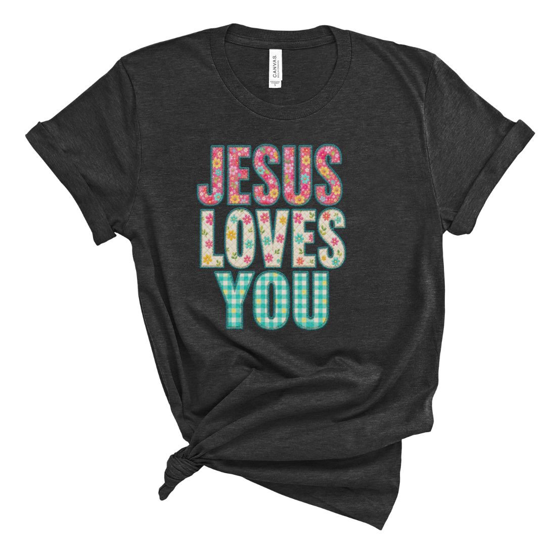 Christian t shirt featuring the phrase Jesus Loves You in colorful floral and gingham patterned letters. Printed faux embroidery and faux quilted patchwork graphic design with a vintage handmade look.