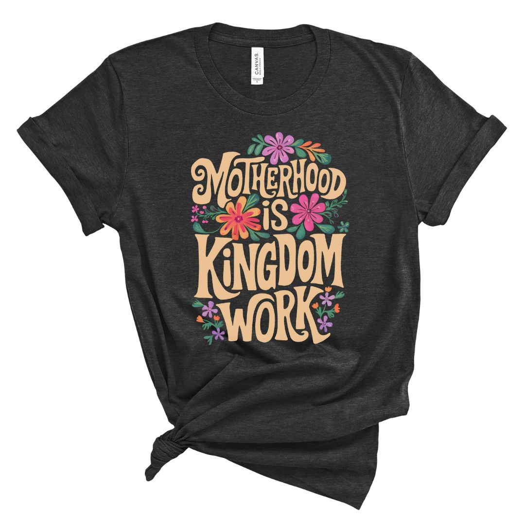A black t-shirt with the text 'Motherhood is KINGDOM WORK' printed in yellow, surrounded by colorful floral designs.
