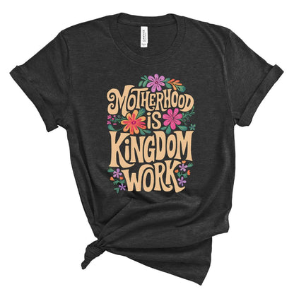 A black t-shirt with the text 'Motherhood is KINGDOM WORK' printed in yellow, surrounded by colorful floral designs.