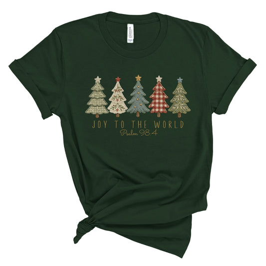 A dark forest green short-sleeve t-shirt with a knotted hem, featuring a graphic of five patterned Christmas trees and the text 'JOY TO THE WORLD Psalm 98' printed on the chest.