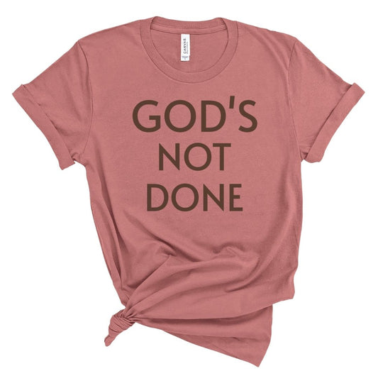 Pink t-shirt with 'GOD'S NOT DONE' text on a white background