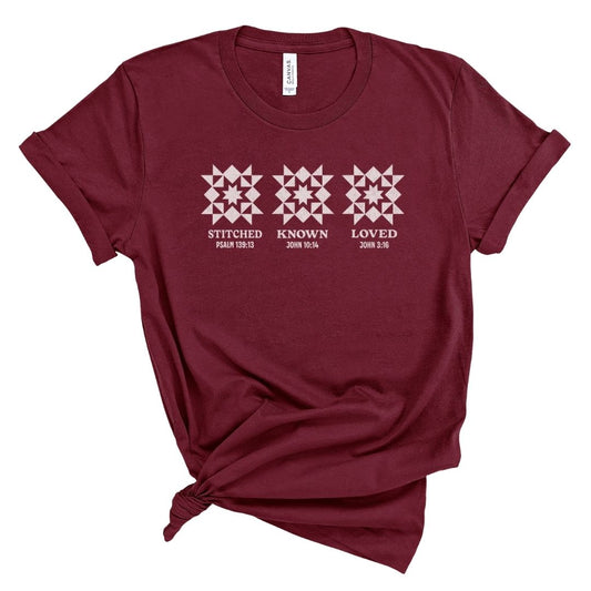 Christian shirt for women featuring quilt-style stitched symbols with the words Stitched Known Loved and Scripture references Psalm 139:13, John 10:14, and John 3:16