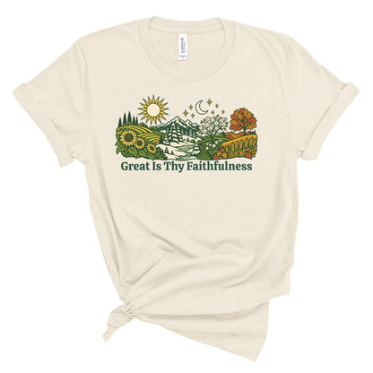 An off-white short-sleeve t-shirt with a graphic of a scenic landscape and the text 'Great Is Thy Faithfulness' printed on the front, styled with a knot at the bottom hem.