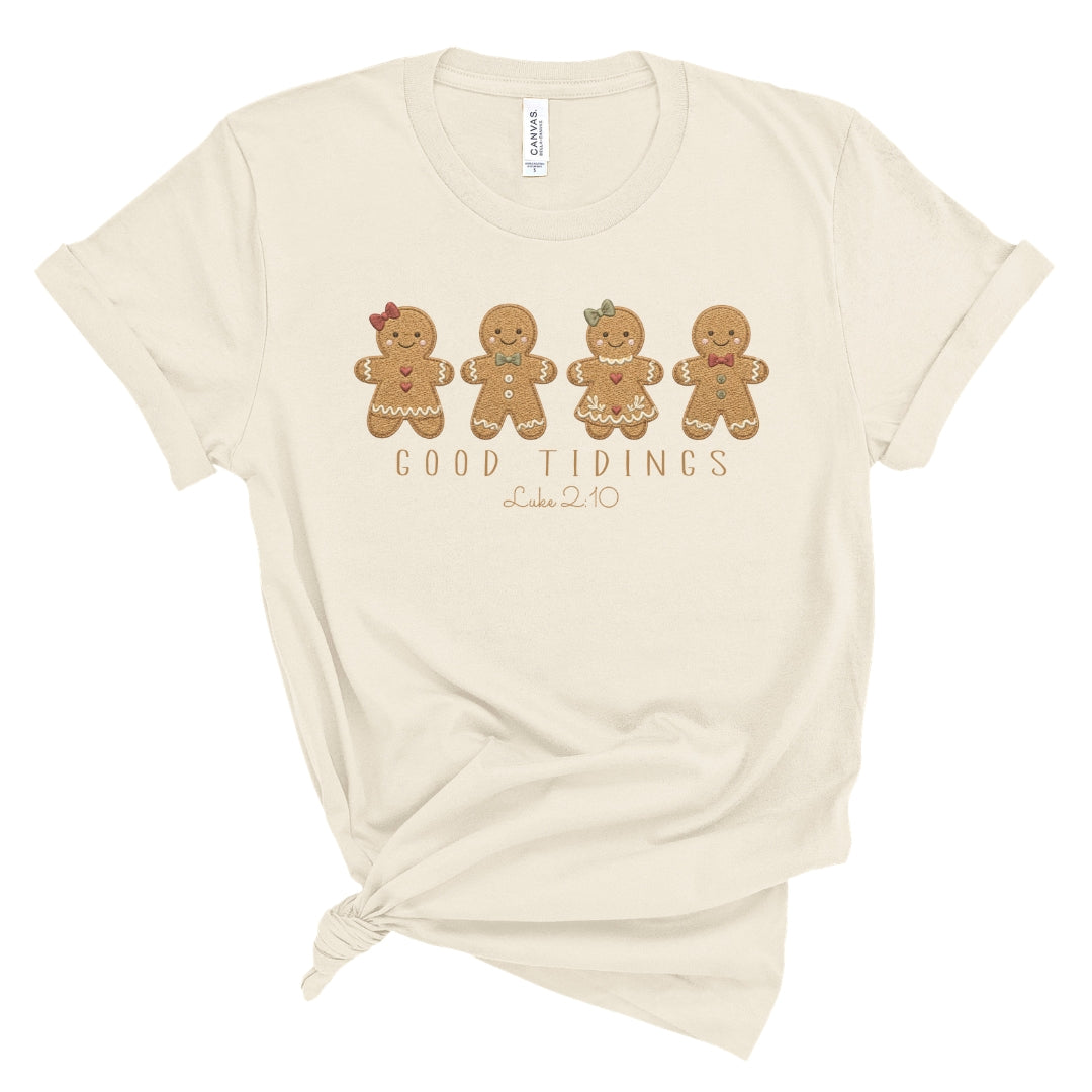 Christian Christmas tee with four gingerbread characters in a printed faux embroidery style, with Good Tidings and Luke 2:10 underneath.