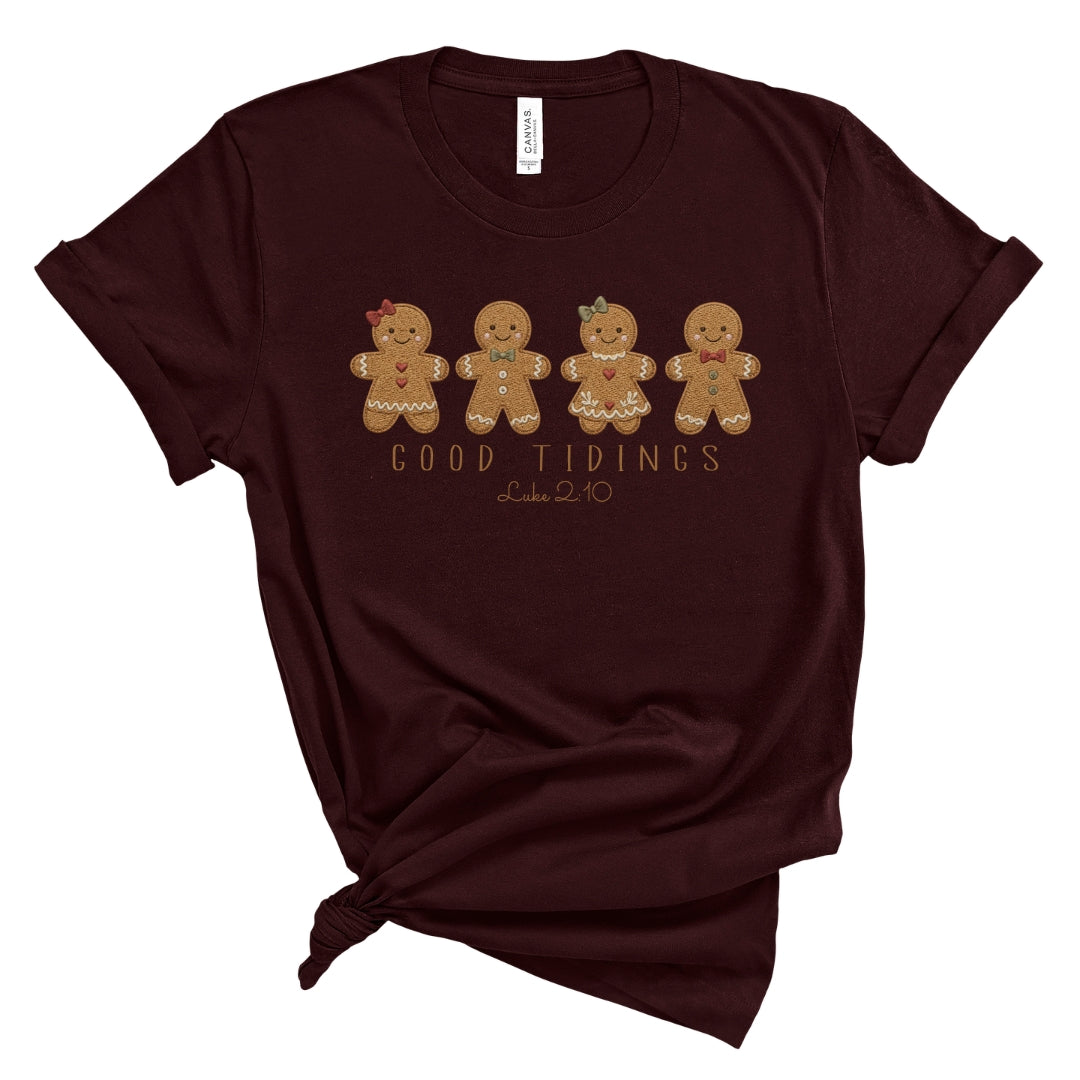 Christian Christmas tee with four gingerbread characters in a printed faux embroidery style, with Good Tidings and Luke 2:10 underneath.