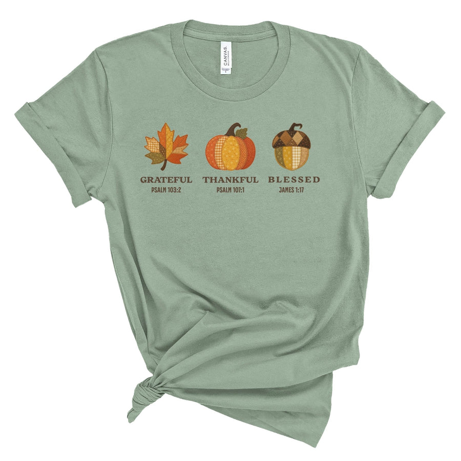 Cream Christian t shirt for women featuring patchwork style fall leaf, pumpkin, and acorn with the words Grateful, Thankful, Blessed and Bible verses Psalm 103:2, Psalm 107:1, and James 1:17.