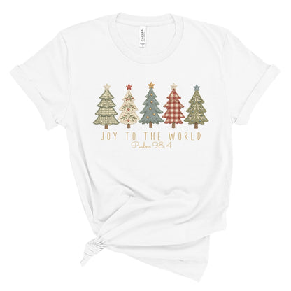 A white short-sleeve t-shirt with a knotted hem, featuring a graphic of five Christmas trees in muted, vintage patterns above the text 'JOY TO THE WORLD Psalm 98:4'.