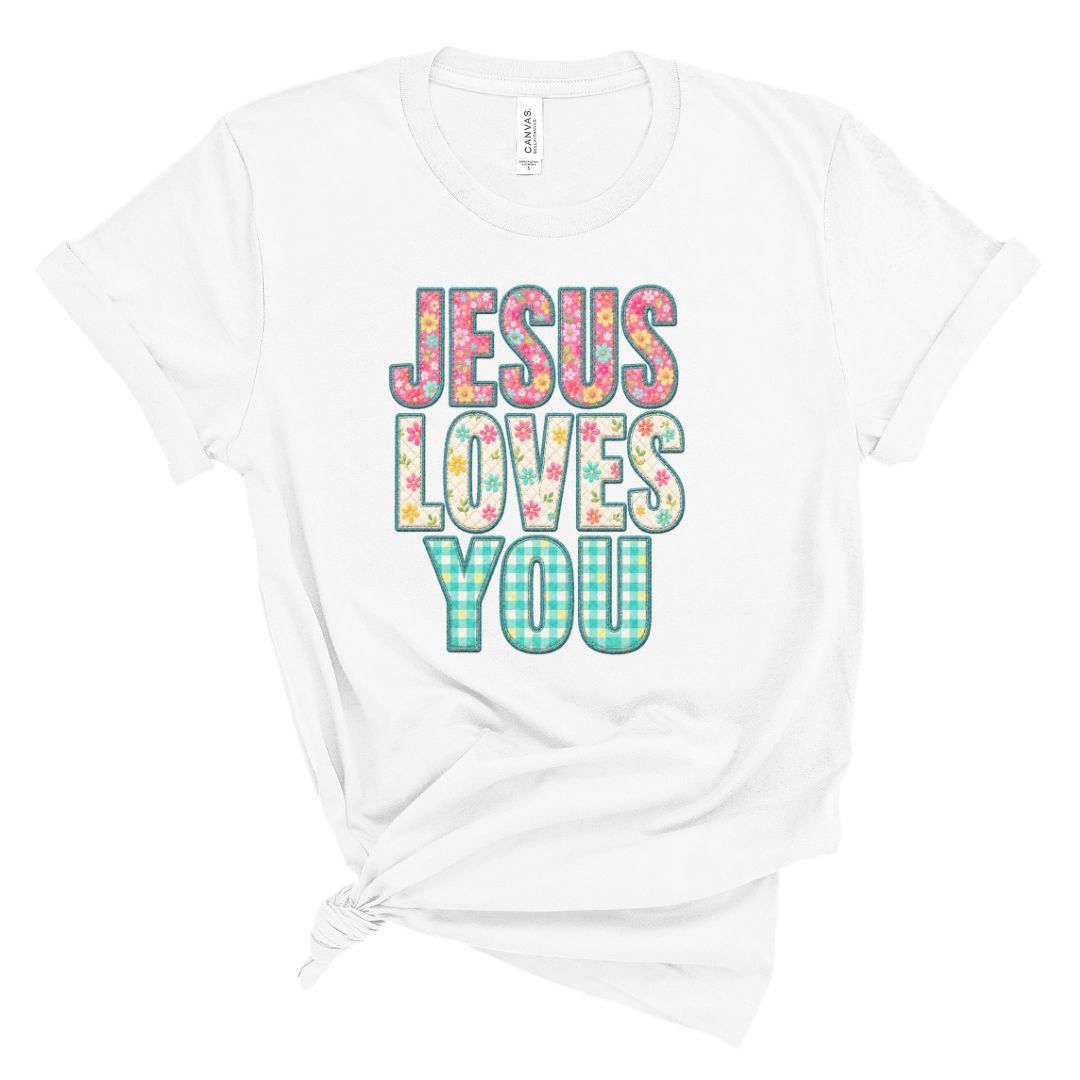 Christian t shirt featuring the phrase Jesus Loves You in colorful floral and gingham patterned letters. Printed faux embroidery and faux quilted patchwork graphic design with a vintage handmade look.