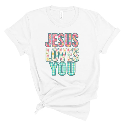 Christian t shirt featuring the phrase Jesus Loves You in colorful floral and gingham patterned letters. Printed faux embroidery and faux quilted patchwork graphic design with a vintage handmade look.
