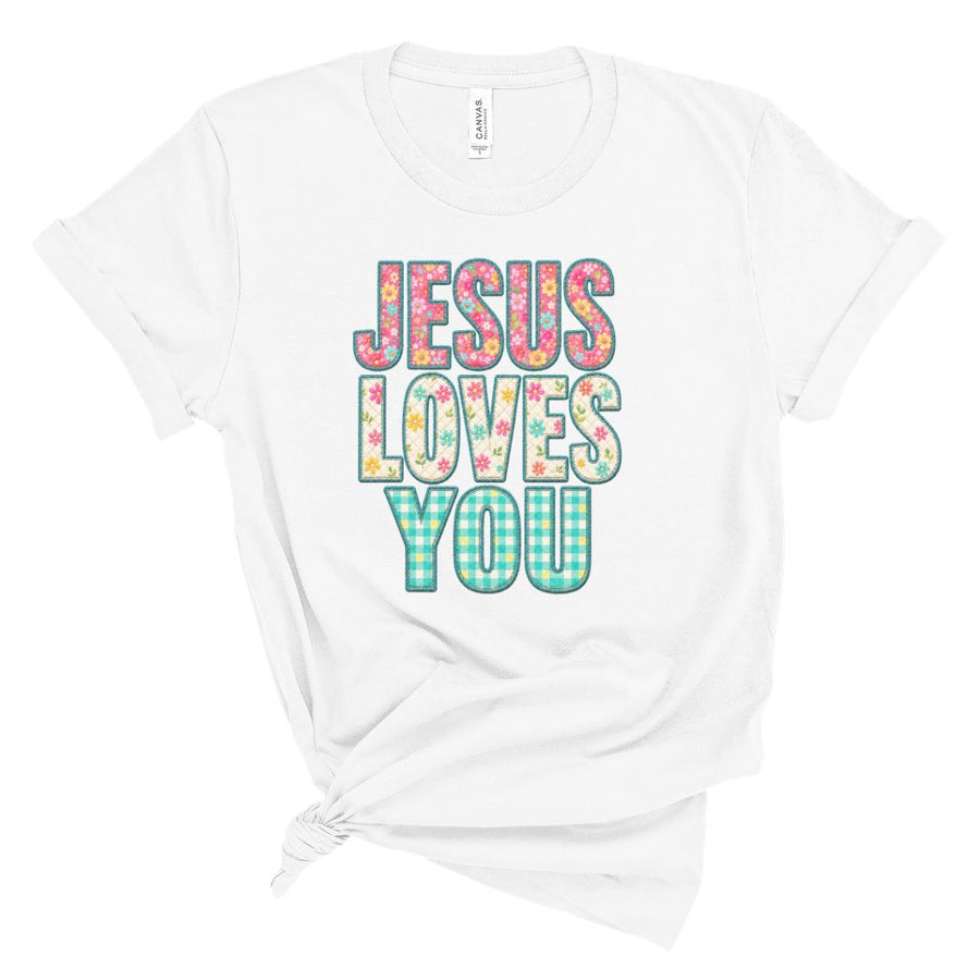 Christian t shirt featuring the phrase Jesus Loves You in colorful floral and gingham patterned letters. Printed faux embroidery and faux quilted patchwork graphic design with a vintage handmade look.